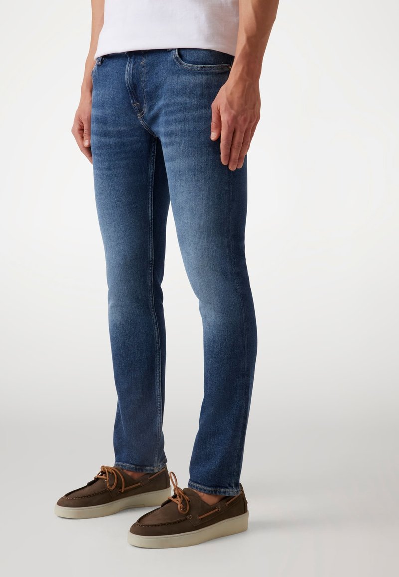 Donkerblauwe skinny jeans met een gladde textuur, vijf-pocket ontwerp en lichte vervaging. Gecombineerd met bruine veterschoenen met een lichte zool.