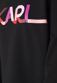 Tissu noir avec « KARL » en grandes lettres blocs multicolores et « LAGERFELD » en petites lettres roses sur le côté droit.
