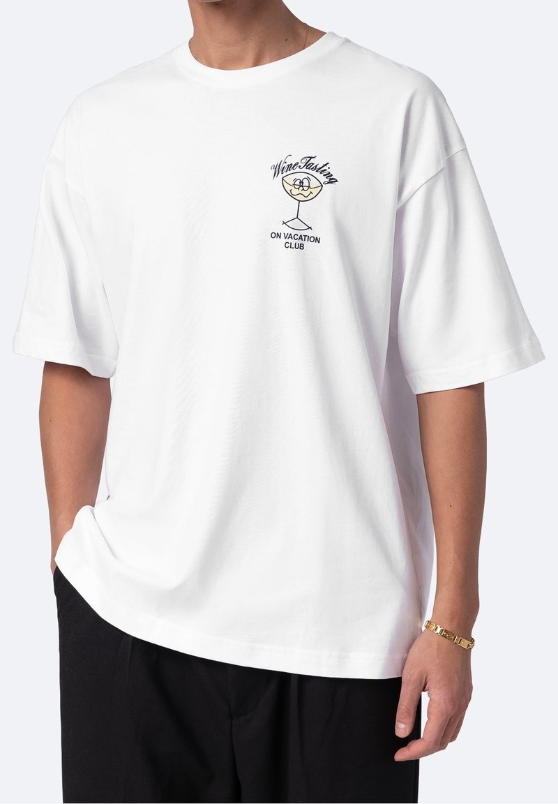 Biała bawełniana koszulka z grafiką kieliszka do wina oraz napisem "Klub Degustacji Wina na Wakacjach" w kolorze czarnym po lewej stronie klatki piersiowej.