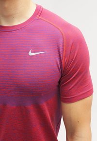 Camisa deportiva de manga corta en tonos degradados de rosa y morado, con rayas horizontales y un pequeño logotipo plateado de Nike en el pecho.