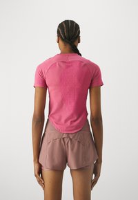 T-shirt de sport rose à manches courtes, avec un design texturé au dos, associé à un short marron avec un ourlet incurvé et des poches.