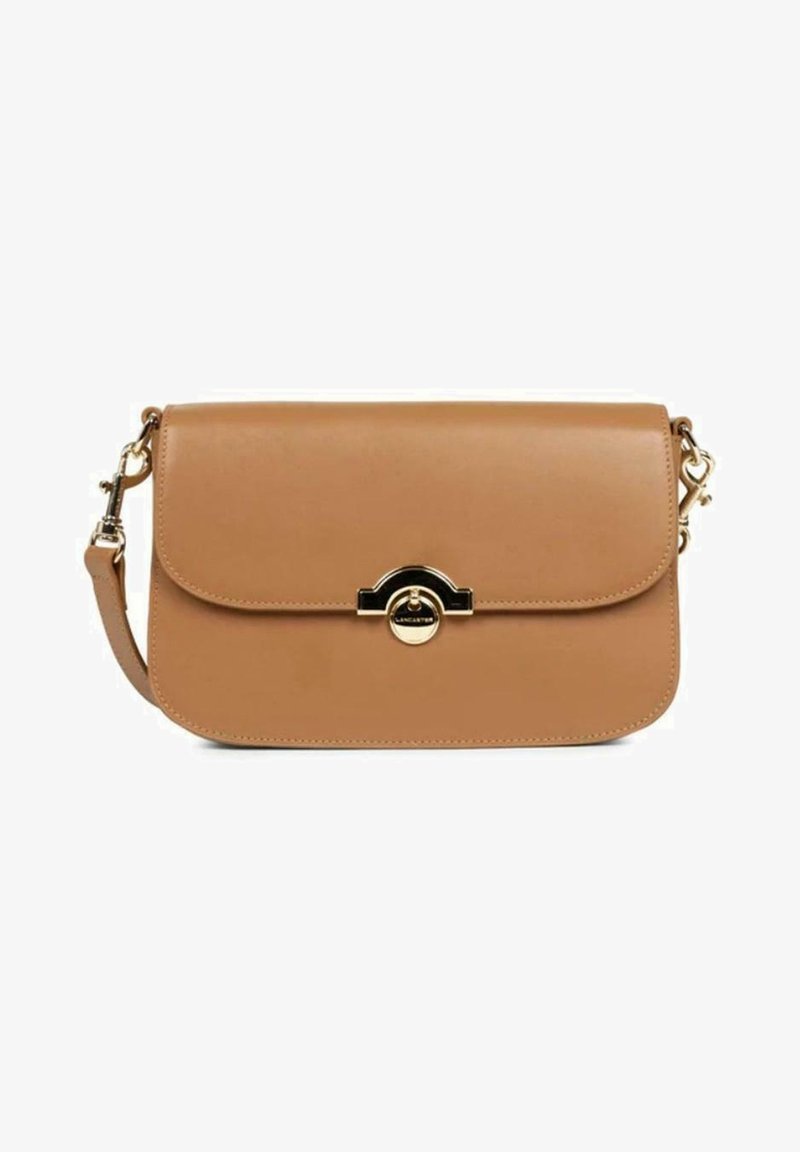 Sac bandoulière en cuir tan avec une fermeture à rabat, quincaillerie dorée et un accent circulaire central. Il est équipé d'une bandoulière amovible.