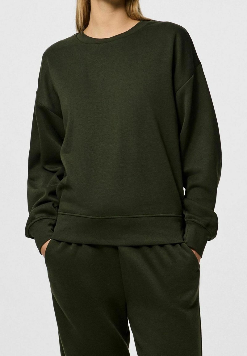 Felpa verde scuro con collo a giro e spalle scese, maniche con polsini a costine. Realizzata in un morbido tessuto testurizzato con una vestibilità comoda.