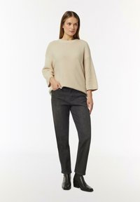 Beige Strickpullover mit weiten Ärmeln, kombiniert mit dunklen Jeans und schwarzen, hohen Stiefeletten. Einfaches Design ohne Muster.