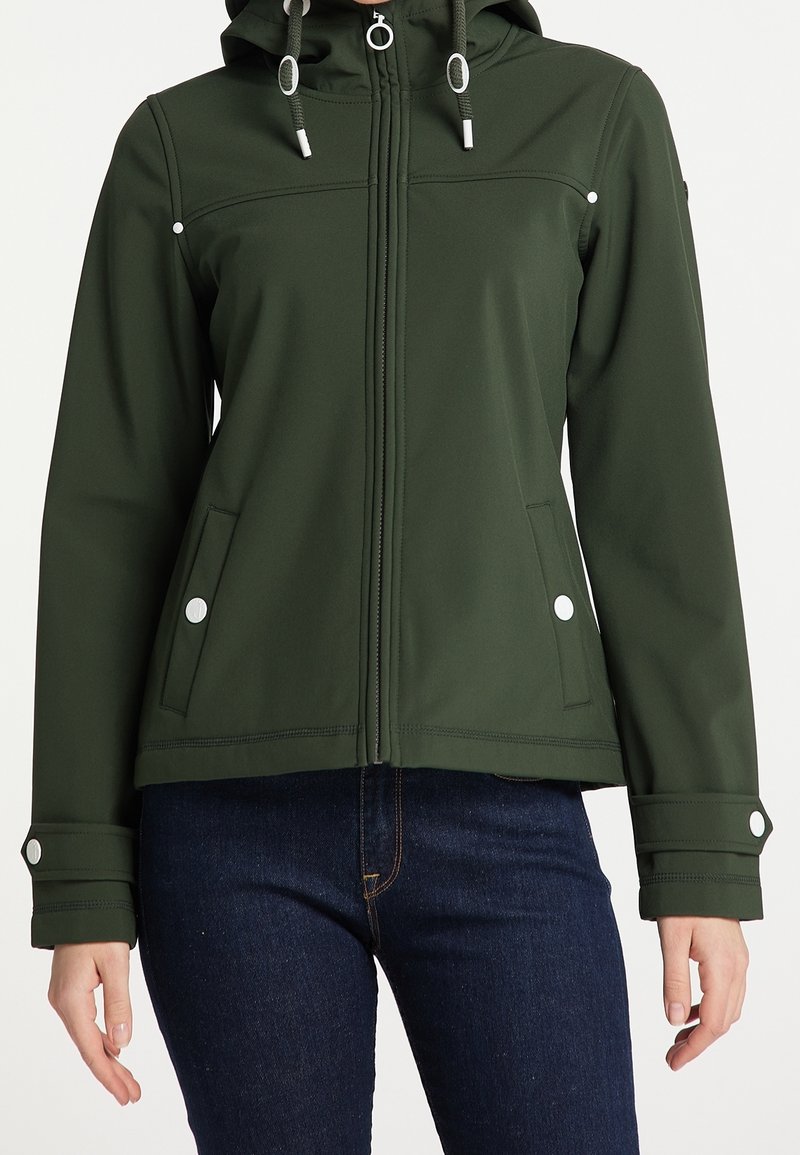 Veste à capuche verte foncée zippée, avec cordons, poches à boutons-pression et poignets à boutons-pression, portée avec un jean bleu foncé.