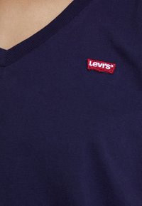 Mörkblå t-shirt med V-krage i bomull med en texturerad yta. Har en röd Levi's-logotyp broderad på vänster bröst.