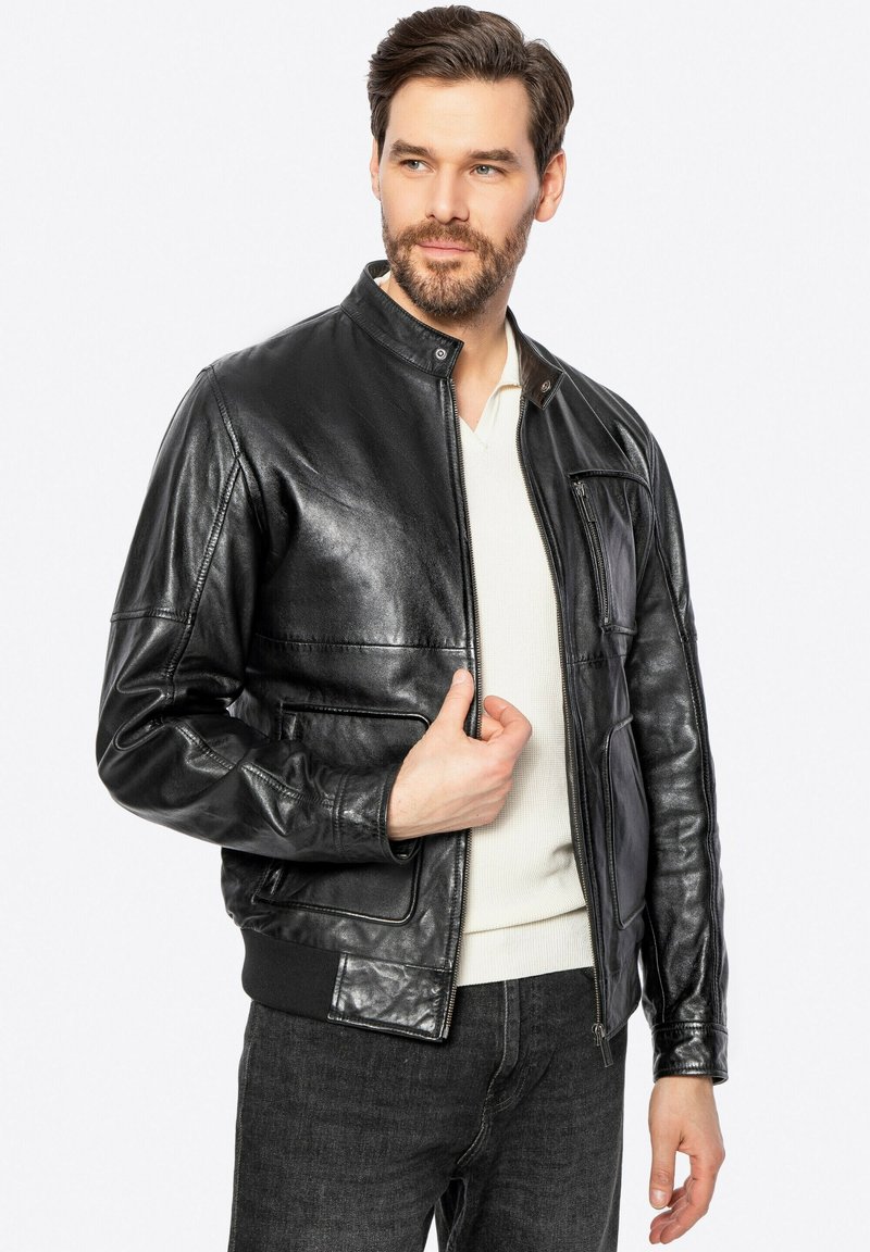 Chaqueta bomber de cuero negro con cuello alzado, cierre de cremallera y bolsillos laterales. Presenta una textura suave y puños de canalé ajustados.