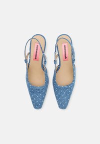 Blue denim slingback shoes with a pointed toe, textured fabric, and adjustable straps. Features a contrasting pink logo on the insole.