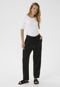 Haut blanc à manches courtes, pantalon noir à jambes larges avec taille à cordon, et sandales noires. Tissu lisse et design minimaliste.
