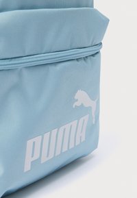 Ανοιχτογάλαζο σακίδιο πλάτης από ανθεκτικό ύφασμα, με εμφανές λευκό λογότυπο Puma και λεπτομέρεια φερμουάρ στο πάνω μέρος. Συμπαγής και δομημένος σχεδιασμός.