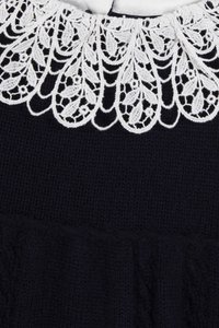 Čierny pletený materiál s bielym čipkovým golierom, ktorý sa vyznačuje zložitými vzormi listov a kvetov.