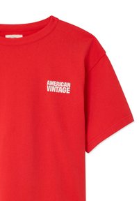 T-shirt rouge à manches courtes avec texte blanc "AMERICAN VINTAGE" imprimé sur le haut à gauche de la poitrine.