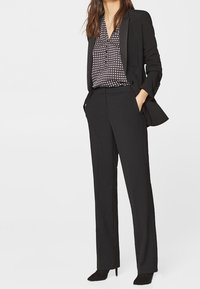 Sort skræddersyet jakkesæt med en tætsiddende blazer og lige bukser; parret med en mønstret bluse. Blødt stof; slankt design.