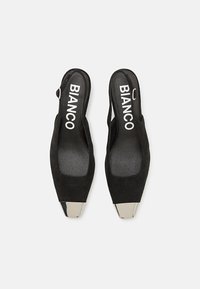 Scarpe slingback nere in suede con punta affilata, caratterizzate da un'accattivante accentatura metallica sulla punta e dal logo sulla soletta.