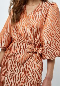 En orange och krämfärgad satin-wrapklänning med tigerstripe-mönster, som har korta puffärmar, knytskärpa i midjan och v-ringning.