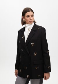 Blazer nero doppiopetto con decorazioni in perline e ricami in oro e blu. Presenta un colletto a punta e tasche frontali.