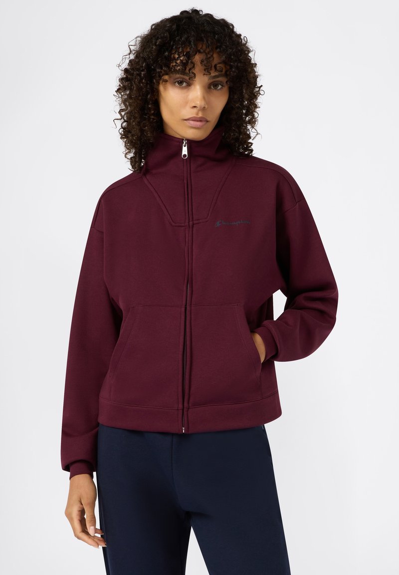 Felpa bordeaux con alto colletto, chiusura a zip, tasche frontali e un logo discreto. Realizzata in morbido tessuto testurizzato per un comfort ottimale.