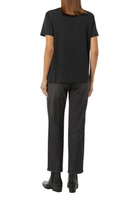 Black cotton T-shirt with short sleeves, paired with dark, slightly textured denim jeans. Black ankle boots complete the outfit.