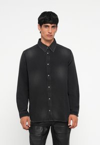 Chemise en denim noir avec un col pointu, des coutures contrastantes et une fermeture à boutons sur le devant. Manches longues avec des poignets à bouton.