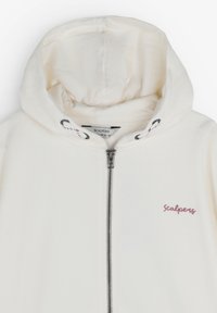 Witte zip-up hoodie met een strakke capuchon, zilveren rits en een roze geborduurd "Scalpers" logo op de borst. Zachte stoftextuur.
