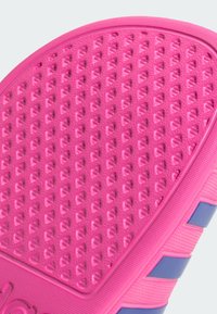 Pink rubber sole with textured pattern of small triangular shapes. Side accents in blue with horizontal stripes.