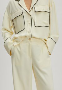 Ensemble de loungewear de couleur crème comprenant une chemise à boutons avec des bordures noires et deux poches poitrine, accompagnée d'un pantalon doux assorti.