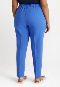 Blå, stretchiga byxor med elastisk midja; slät textur, insvängd design och ankellång nederkant; bärs med platta sandaler.