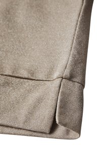 Beige stickad tyg med silvermetallictrådar som visar en vikt manschett och sömdetalj på en ärm.