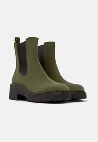 Stivali alla caviglia in suede verde oliva con pannelli laterali elasticizzati, suola nera spessa e un tassello sul tallone per una facile indossabilità. Texture spessa e resistente.