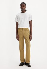 Chino khaki cu un croi drept, realizat din bumbac, având o textură netedă și bucle pentru curea, asortat cu un tricou alb simplu.