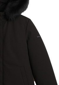 Cappotto invernale nero con cappuccio rifinito in pelliccia, tasca laterale e un'etichetta di marca rettangolare piccola sulla manica superiore.