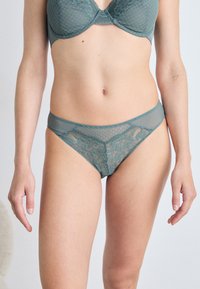Teal blonde og mesh undertøysett med en balconette bh med prikkete mønster og matchende gjennomsiktig stringtruse med blomstrete detaljer.