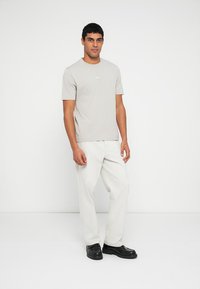 Tricou gri din bumbac cu gât rotund și mâneci scurte, asortat cu pantaloni albi și pantofi negri, expus pe un fundal neutru.