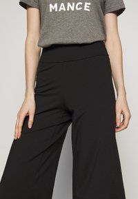 Black wide-leg pants made of a soft, stretchy fabric with an elastic waistband and side pockets, styled with a gray graphic tee.