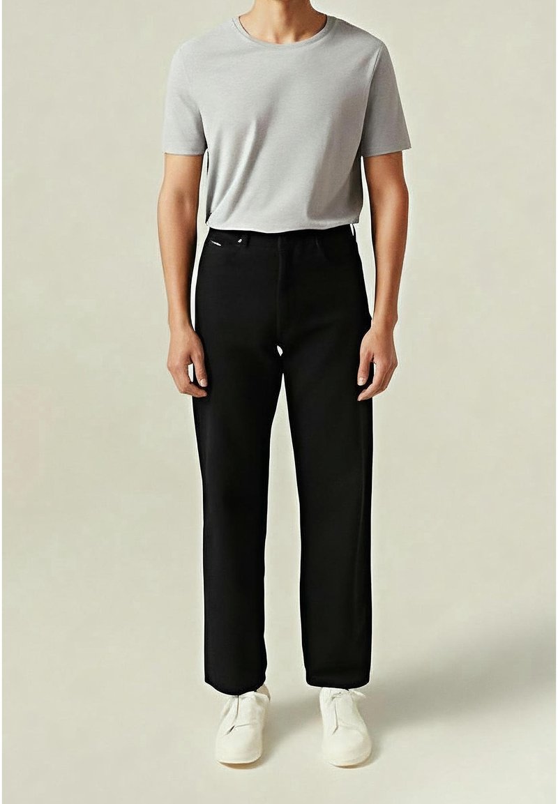 Camiseta gris de manga corta combinada con pantalones rectos negros y zapatillas blancas. El conjunto presenta un diseño simple y minimalista.