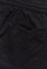 Zbliżenie czarnego materiału z elastycznym pasem i przeszytym prostokątnym detalem kieszeni na plecach.