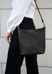 Schwarze Leder-Umhängetasche mit glatter Oberfläche, rechteckiger Form und Reißverschluss. Verfügt über Messingbeschläge und einen abnehmbaren Tragegurt.