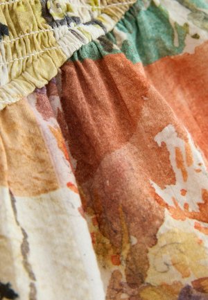 Detail látky s nařaseným elastickým pasem a vícebarevným abstraktním květinovým vzorem v zemních tónech.