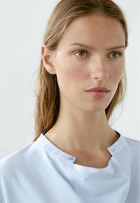 Lichtblauwe, gesloten blouse met een ronde hals. Gemaakt van soepel materiaal, heeft het een subtiele textuur en minimalistische ontwerpelementen.