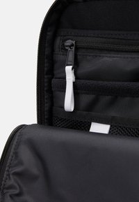 Svart dragkedjeväska med inre fack, inklusive ett meshfack, tygöglor och släta, strukturerade ytor.