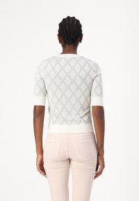 Strickpullover in Hellgrau mit strukturiertem Rautenmuster, kurzen Ärmeln und einem weißen Rippabschluss. Getragen mit hellrosa enganliegenden Jeans.