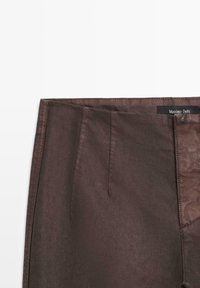 Braune Stoffhose mit glatter Textur, maßgeschneiderter Schnitt, Vorderfalten und einem dezenten Etikett am Bund.