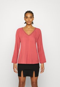 Top de mangas longas cor-de-rosa com decote em V e mangas largas, combinado com uma saia mini preta com aberturas frontais. Textura suave.