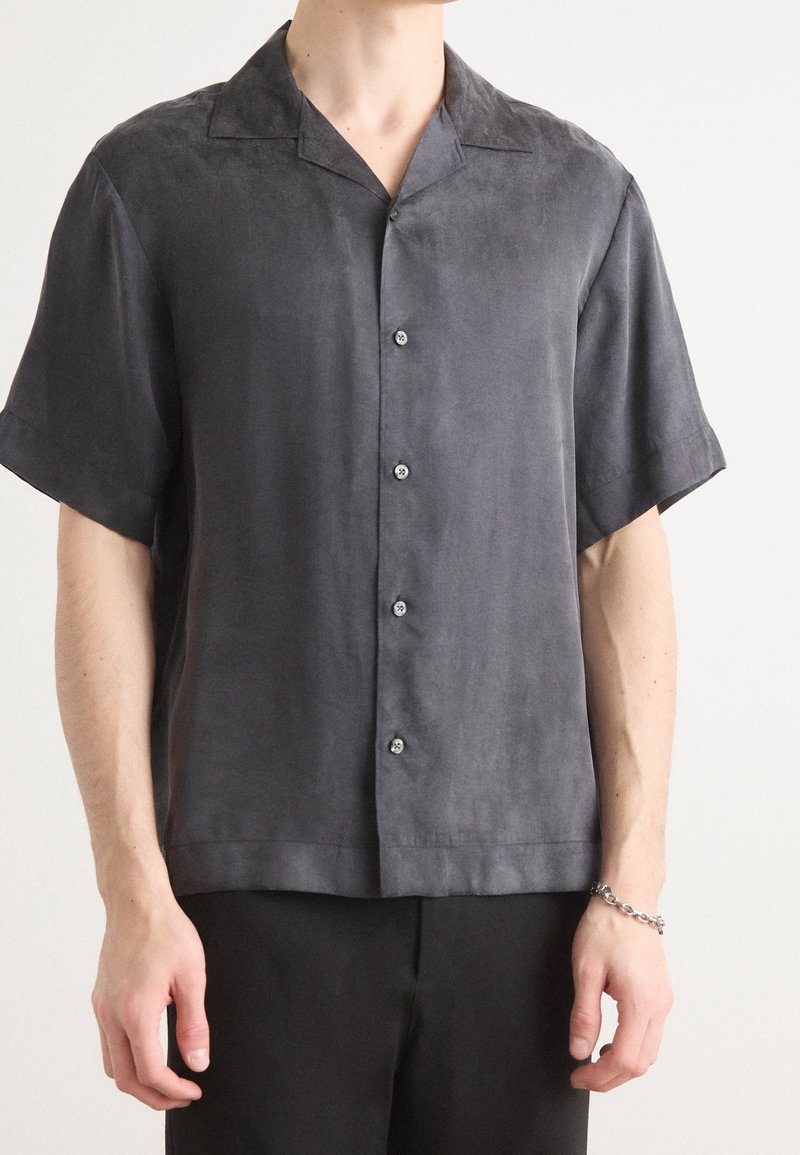 Camisa de manga corta en gris oscuro, de tejido ligero con cuello y cinco botones, y una textura suave. Diseño limpio y minimalista.