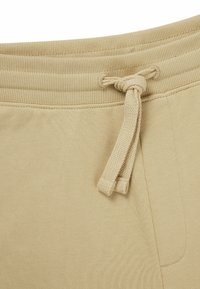 Beige katoenen sweatpants met een geribde tailleband en een trekkoord. Heeft een gladde structuur en een zijzak aan de rechterkant.