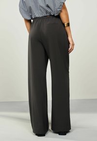 Pantaloni a gamba larga di colore grigio scuro, realizzati in un tessuto liscio. Vita elasticizzata e tasca posteriore singola. Abbinati a una maglietta a righe.