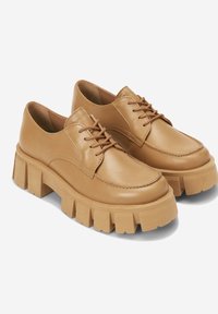 Chaussures en cuir tan avec un bout rond, des lacets droits et une semelle épaisse à plateforme présentant de profondes rainures pour la texture et l'adhérence.