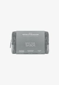 Trousse cosmétique en maillage argenté avec une étiquette grise et du texte blanc. Contient trois produits de soin : sérums et crème, indiqués sur l'étiquette.