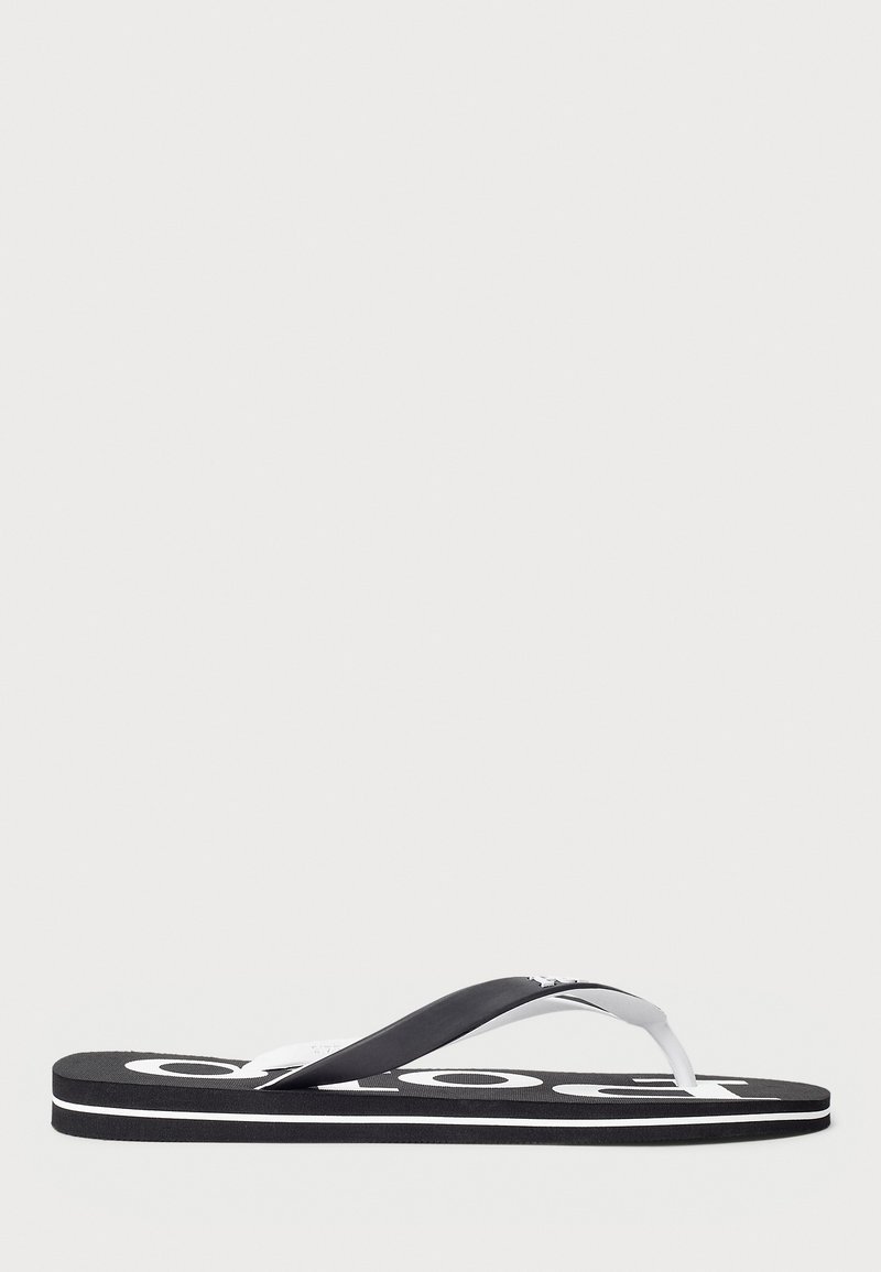 Chancla en blanco y negro con suela gruesa de acabado texturizado y un logo en la plantilla; tiras delgadas y flexibles para mayor comodidad.