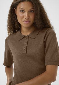Barna, rövidujjú polóing, texturált anyagból készült, klasszikus gallérral és öt gombos záródással a nyaknál.